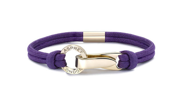 <strong>Asprey｜アスプレイ</strong>　コットンコードの色はシックなブラックとコーポレートカラーのパープルから、地金はイエローゴールドとシルバーから組み合わせを選べる。「Aライン リストバンド」[YGクラスプ×パープルコットンコード] 36万5000円（アスプレイ／アスプレイ ジャパン）